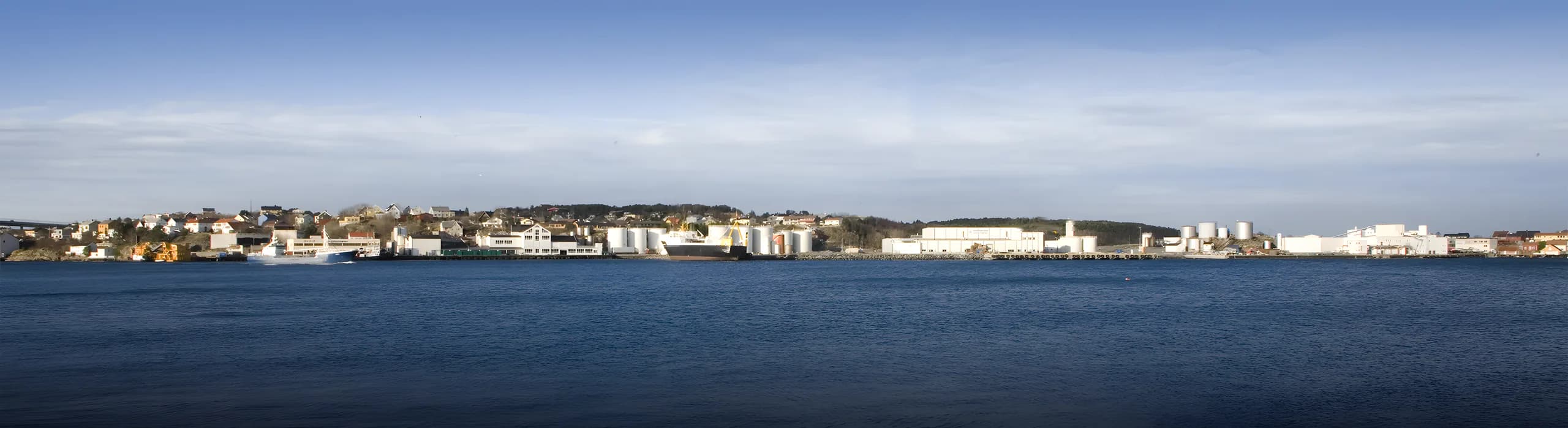 Norwegian coastal industrial waterfront, fishing vessels, cargo ships and tank storage along the fjord under a wide arctic sky